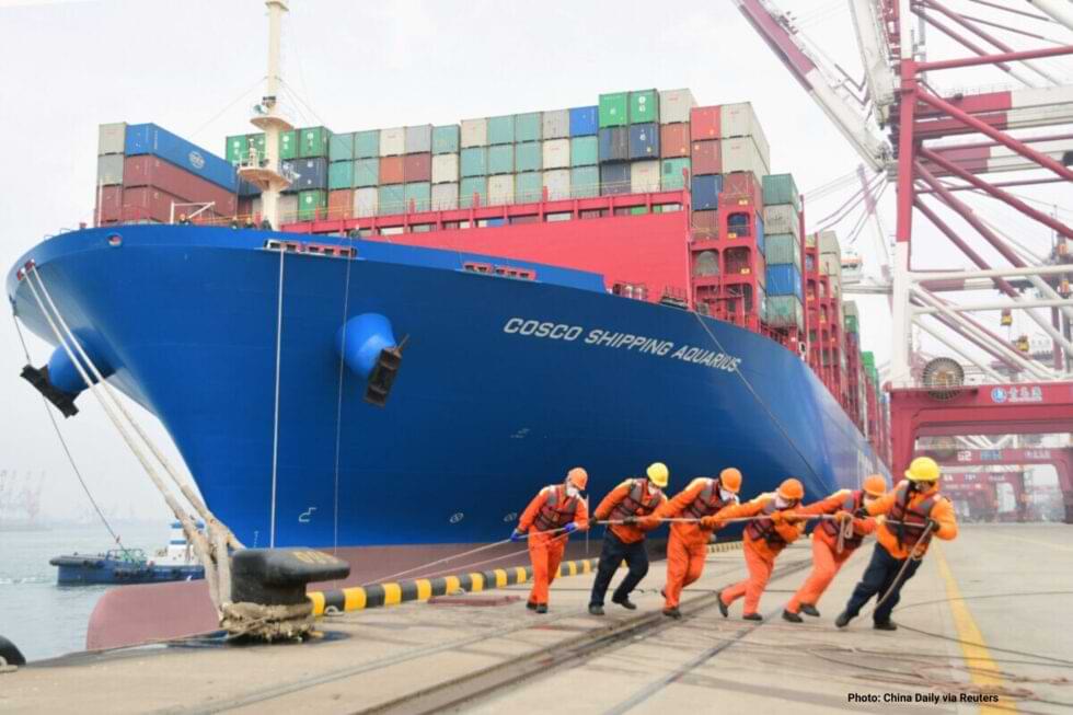 A group of 3 workmen pulling the rope of a ship anchor representing supply chain constrains on global markets due to covid-19.